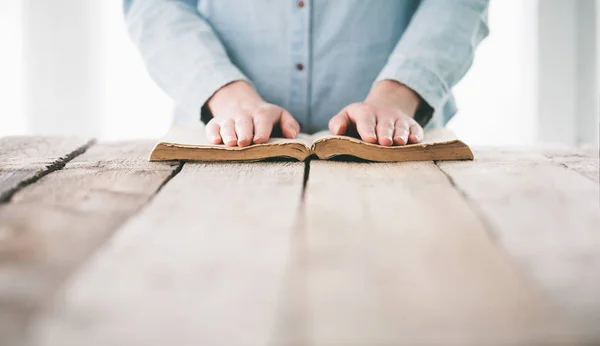 Hands praying with a bible over wooden table — Stock Photo, Image