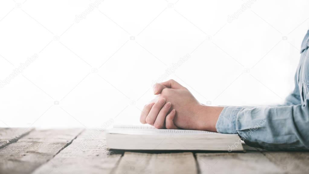 hands praying with a bible over wooden table