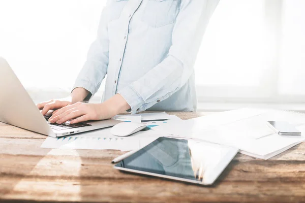 Frau arbeitet drinnen an Laptop und Tablet-PC auf einem Holzständer — Stockfoto