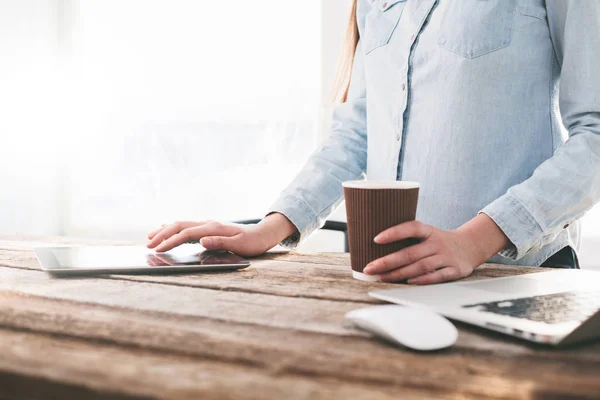 Frau arbeitet drinnen an Laptop und Tablet-PC auf einem Holzständer — Stockfoto