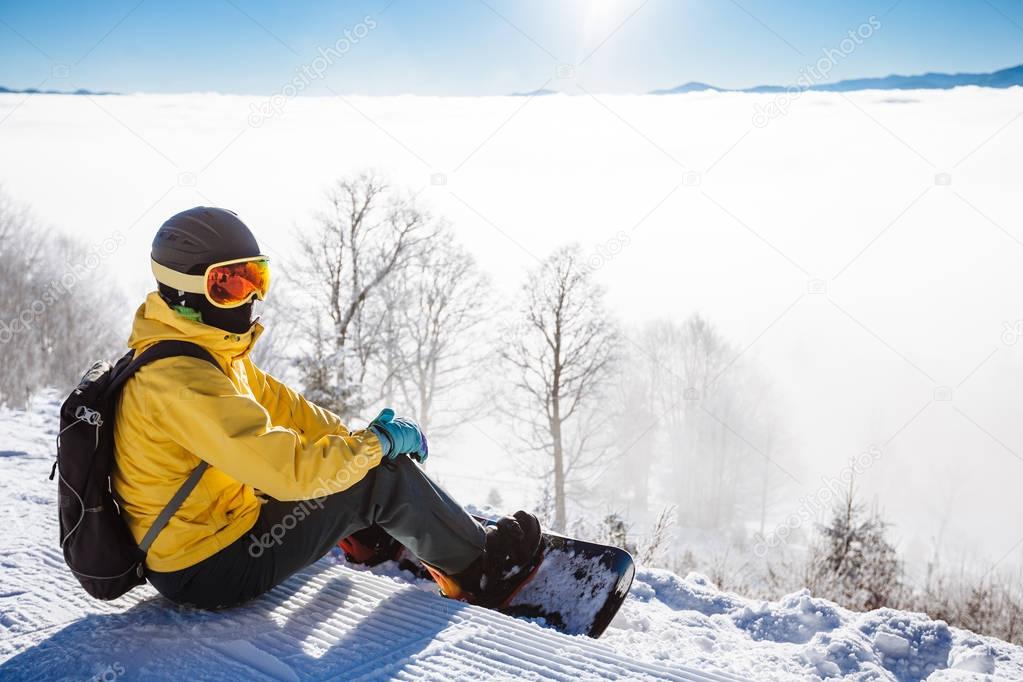 Snowboarder sitting and looking at mountain chain in the backgro