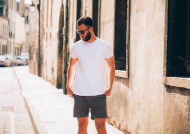 Hipster handsome male model with beard wearing white blank t-shirt with space for your logo or design in casual urban style clipart