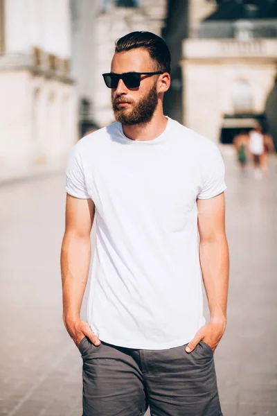 Hipster tampan model laki-laki dengan jenggot mengenakan putih kosong t-shirt dengan ruang untuk logo atau desain dalam gaya perkotaan kasual — Stok Foto