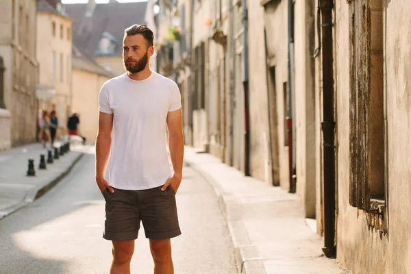 Hipster guapo modelo masculino con barba que lleva una camiseta blanca en blanco con espacio para su logotipo o diseño en estilo urbano casual — Foto de Stock