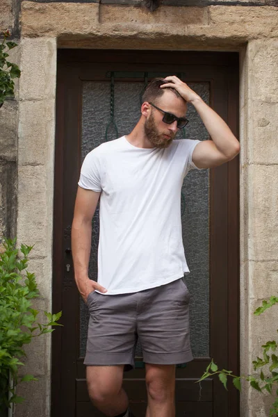 Hipster handsome male model with beard wearing white blank t-shirt with space for your logo or design in casual urban style — Stock Photo, Image