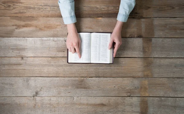 Manos de mujer sosteniendo una biblia sobre un escritorio . — Foto de Stock