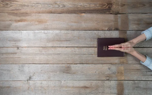 Handen van de vrouw met een Bijbel over een bureau. — Stockfoto