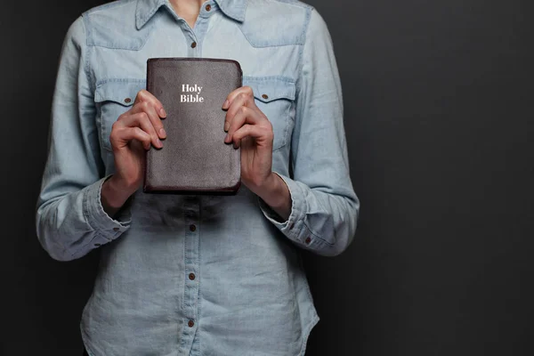 Woman holding a Bible in hands over the gray background — Stock Photo, Image