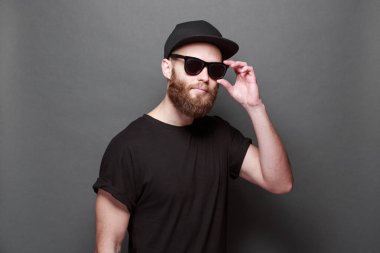 Hipster yakışıklı erkek model gri arka plan üzerinde logo veya tasarım alanı olan siyah boş t-shirt giyen sakallı