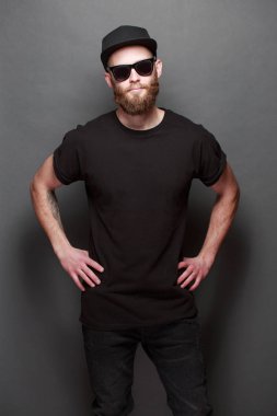 Hipster yakışıklı erkek model gri arka plan üzerinde logo veya tasarım alanı olan siyah boş t-shirt giyen sakallı