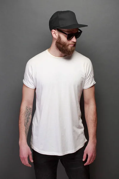 Modelo masculino bonito Hipster com barba vestindo t-shirt branca em branco com espaço para o seu logotipo ou design sobre fundo cinza — Fotografia de Stock