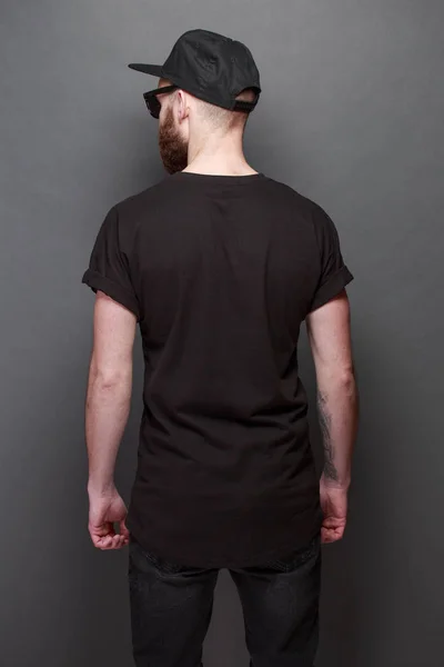 Hipster model mężczyzna przystojny z brodą noszenia czarny t-shirt puste z miejscem na logo firmy lub projektu na szarym tle — Zdjęcie stockowe
