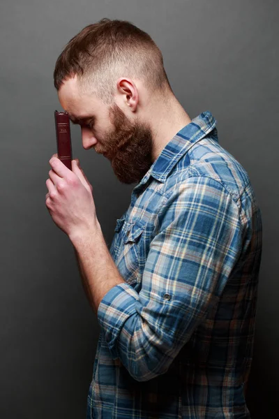 Handsone man reading and praying over Bible in a dark room over gray texture — Stock Photo, Image