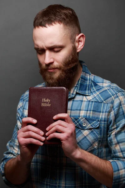 Handsone man läsa och be över Bibeln i ett mörkt rum över grå textur — Stockfoto