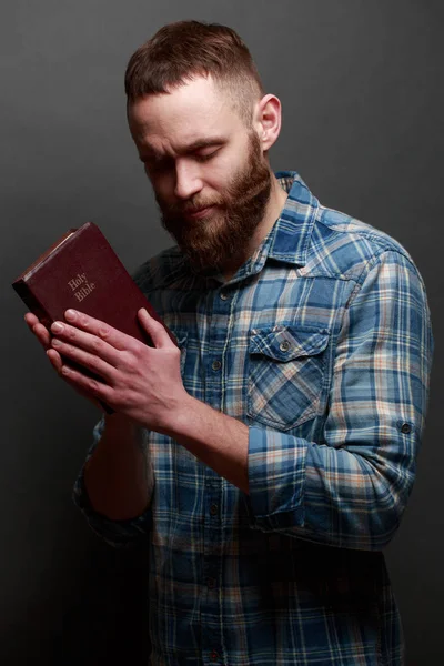 Handsone man reading and praying over Bible in a dark room over gray texture — Stock Photo, Image