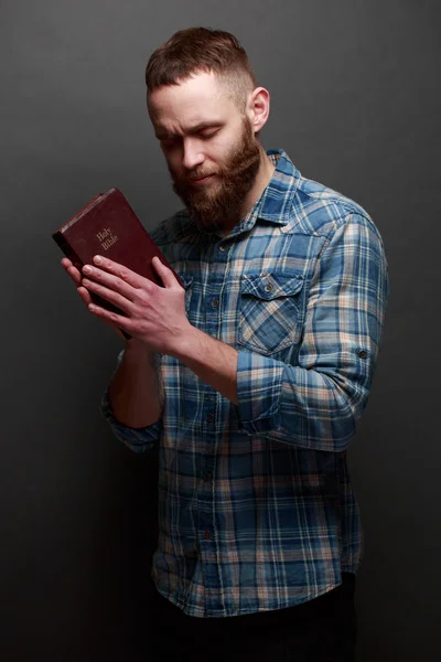 Handsone muž pevny nad Bibli v temné místnosti nad tmavošedá textura — Stock fotografie