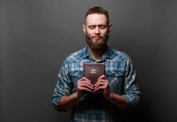 Handsone man reading and praying over Bible in a dark room over gray texture — Stock Photo, Image