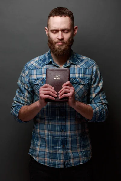 Homem Handsone lendo e orando sobre a Bíblia em um quarto escuro sobre a textura cinza — Fotografia de Stock