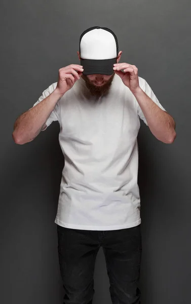 Hipster handsome male model with beard wearing white blank t-shirt and a baseball cap with space for your logo or design in casual urban style — Stock Photo, Image