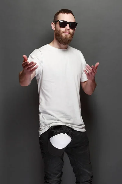 Hipster guapo modelo masculino con barba vistiendo camiseta blanca en blanco y una gorra de béisbol con espacio para su logotipo o diseño en estilo urbano casual — Foto de Stock