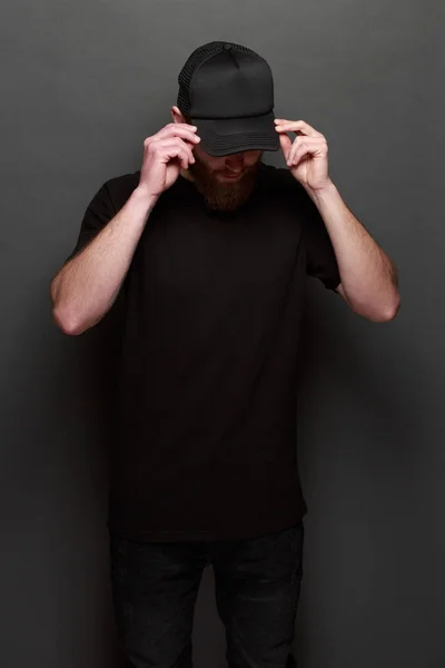 Hipster gutaussehendes männliches Model mit Bart trägt ein schwarzes Blank-T-Shirt und ein schwarzes Basecap mit Platz für Ihr Logo oder Design im lässigen urbanen Stil — Stockfoto