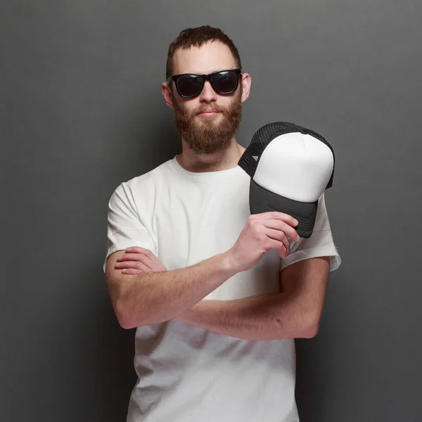 Modelo masculino bonito Hipster com barba vestindo t-shirt branca em branco e um boné de beisebol com espaço para o seu logotipo ou design em estilo urbano casual — Fotografia de Stock