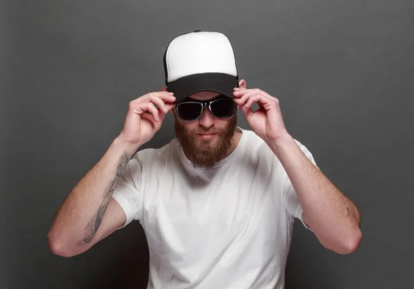 Sakallı, beyaz, boş tişörtlü, beysbol şapkalı, logonuz için yeri olan yakışıklı bir hippi mankeni. — Stok fotoğraf
