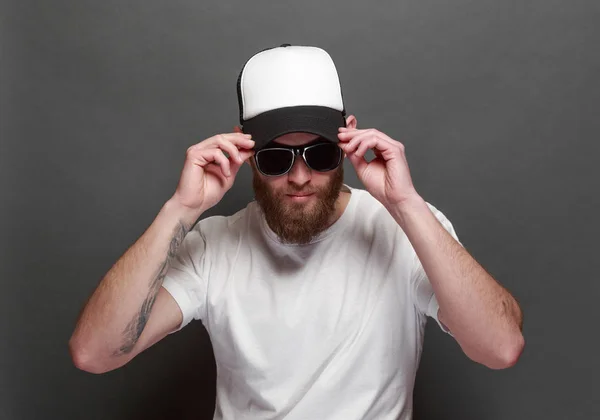 Hipster handsome male model with beard wearing white blank t-shirt and a baseball cap with space for your logo or design in casual urban style — Stock Photo, Image