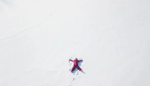 Niña jugando y haciendo un ángel de nieve en la nieve. Plano superior — Foto de Stock