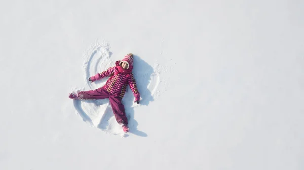 Bambina che gioca e fa un angelo della neve nella neve. Vista aerea superiore piatta — Foto Stock