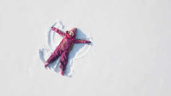 Dziewczynka bawi się i robi śnieżnego anioła w śniegu. Górny płaski widok nad głową — Zdjęcie stockowe