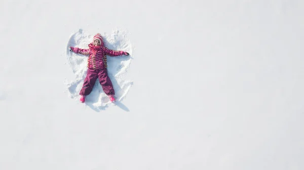 Child girl playing and making a snow angel in the snow. Top flat overhead view