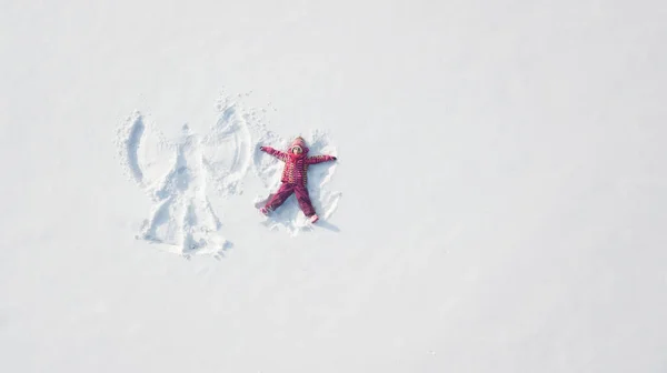 Ребенок играет и делает снежного ангела в снегу. Верхний плоский вид сверху — стоковое фото