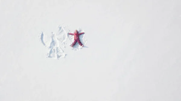 雪の中で遊んで雪の天使を作る子供の女の子。トップフラットオーバーヘッドビュー — ストック写真