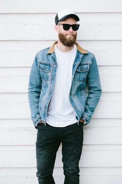 Hipster handsome male model with beard wearing white blank t-shirt and a baseball cap with space for your logo or design in casual urban style — Stock Photo, Image