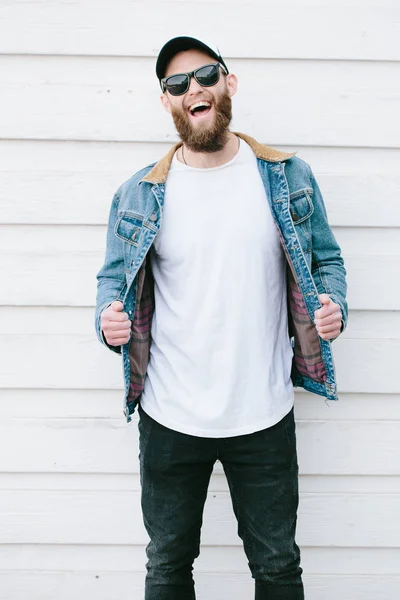 Hipster guapo modelo masculino con barba vistiendo camiseta blanca en blanco y una gorra de béisbol con espacio para su logotipo o diseño en estilo urbano casual — Foto de Stock