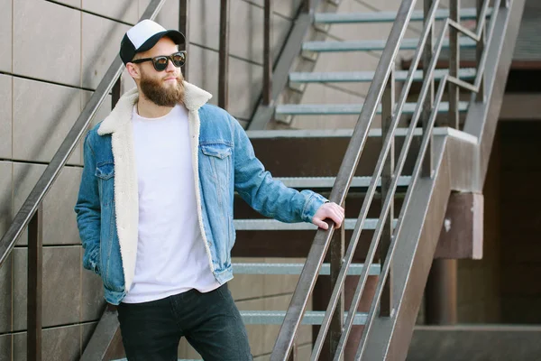 Modelo masculino bonito Hipster com barba vestindo t-shirt branca em branco e um boné de beisebol com espaço para o seu logotipo ou design em estilo urbano casual — Fotografia de Stock