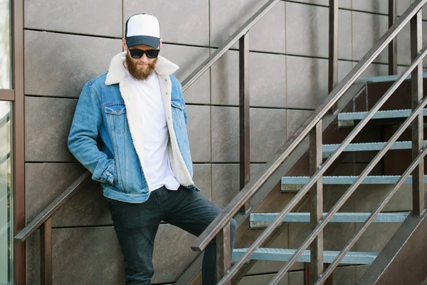 Hipster knappe mannelijke model met baard met witte witte witte t-shirt en een honkbalpet met ruimte voor uw logo of ontwerp in casual stedelijke stijl — Stockfoto