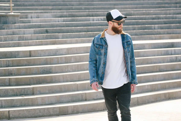 Hipster handsome male model with beard wearing white blank t-shirt and a baseball cap with space for your logo or design in casual urban style — Stock Photo, Image