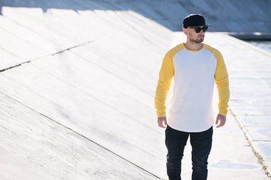 Beyaz ve sarı boş uzun kollu gömlek giyen sakallı bir adam modeli ve logonuz için geniş bir beyzbol şapkası ya da gelişigüzel tasarlanmış bir şehir tarzı.