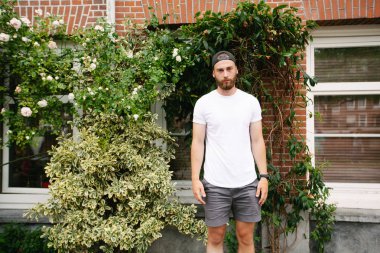 Sakallı, beyaz, boş tişörtlü, beysbol şapkalı, logonuz için yeri olan yakışıklı bir hippi mankeni.