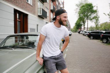 Sakallı, beyaz, boş tişörtlü, beysbol şapkalı, logonuz için yeri olan yakışıklı bir hippi mankeni.