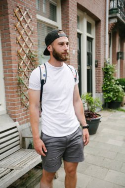 Sakallı, beyaz, boş tişörtlü, beysbol şapkalı, logonuz için yeri olan yakışıklı bir hippi mankeni.