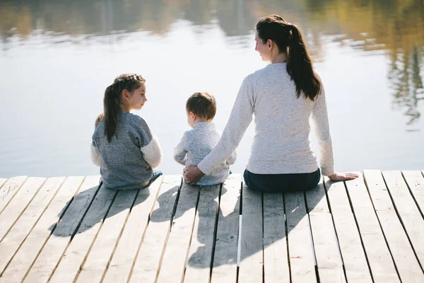 Matka i dzieci relaksujące się nad jeziorem. Uśmiechają się i rozmawiają w słoneczny jesienny dzień — Zdjęcie stockowe