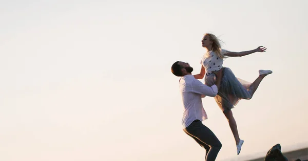Ett par förälskade kramas under solnedgången. Mannen lyfter en flicka. — Stockfoto