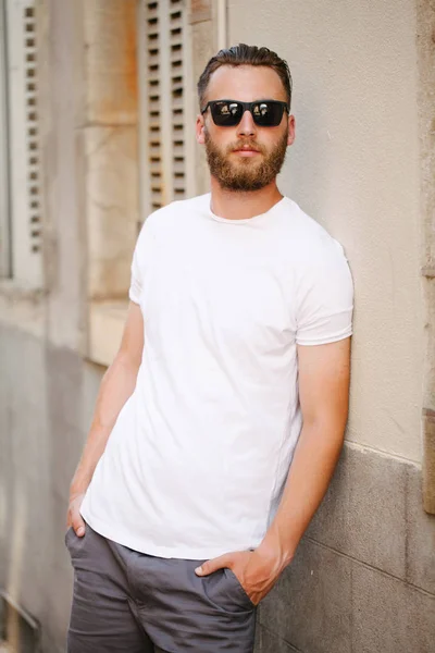 Hipster przystojny model męski z brodą w białym, czystym t-shircie i czapce z daszkiem z miejscem na logo lub projekt w miejskim stylu casual — Zdjęcie stockowe