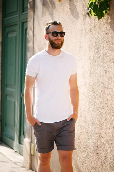 Modelo masculino bonito Hipster com barba vestindo t-shirt branca em branco e um boné de beisebol com espaço para o seu logotipo ou design em estilo urbano casual — Fotografia de Stock