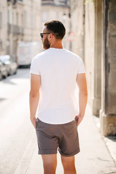 Modelo masculino bonito Hipster com barba vestindo t-shirt branca em branco e um boné de beisebol com espaço para o seu logotipo ou design em estilo urbano casual — Fotografia de Stock