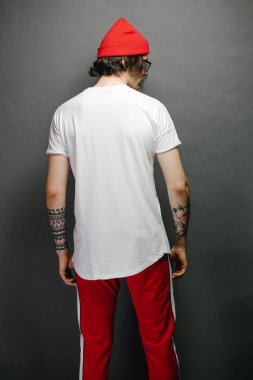 Gözlüklü, beyaz, boş tişörtlü, kırmızı pantolonlu, logonuz için yeri olan kırmızı şapkalı hippi ve yakışıklı bir erkek model.