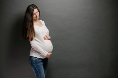 Hamile kadın portresi. Karnını tutuyor ve gülümsüyor.